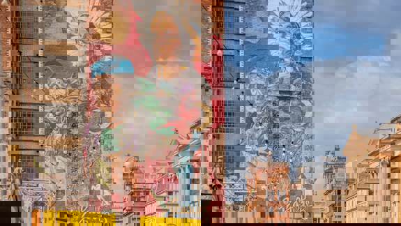 Colourful mural on a brick wall depicting two figures, one with an elaborate feathered headdress.