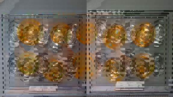 Ten gilded metal plates are displayed in two rows inside a glass case.