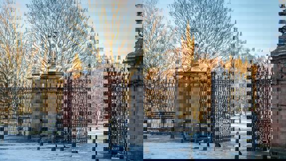 The grand entrance gates of Kelvingrove Park on a frosty winter day, with the University of Glasgow's main building visible through the bare trees in the background.