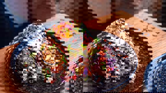 Close-up of a loaded brunch dish with a fried egg, avocado, vegetables, and a grilled lime slice.