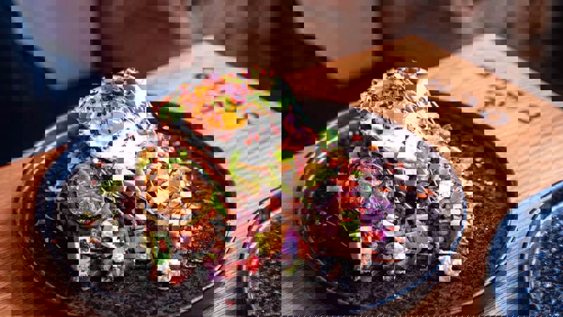 Close-up of a loaded brunch dish with a fried egg, avocado, vegetables, and a grilled lime slice.