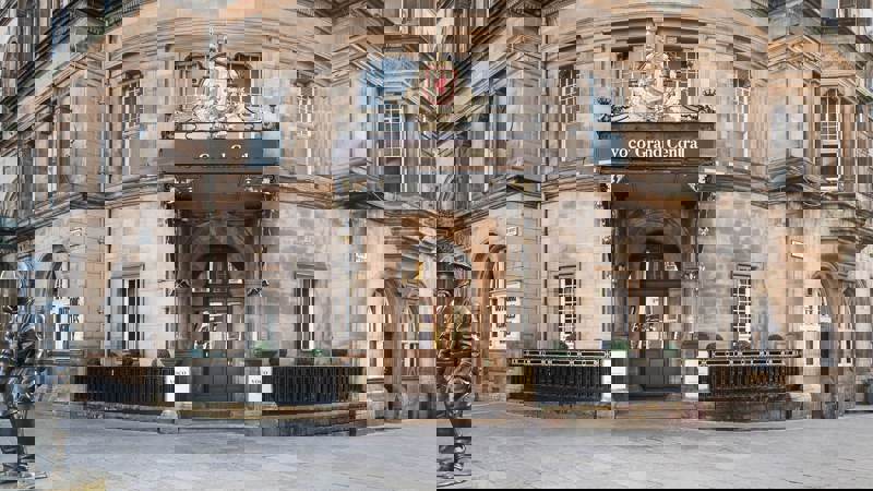 A historic, stone-built hotel in Glasgow, showing a central ornate doorway with a royal crest and a statue of a helmeted figure.