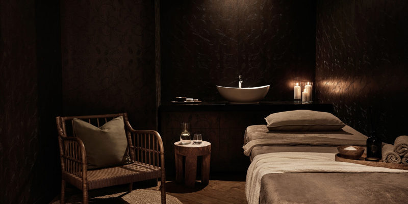 A spa treatment room with a massage bed, soft lighting, wooden panelling.