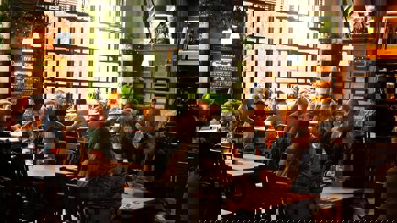 Cozy pub interior with people sitting at wooden tables, talking and drinking beer in a warm, softly lit atmosphere with plants by large windows