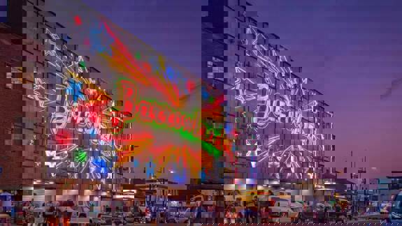 The illuminated "Barrowland" sign glows in a vibrant neon red and green as people walk on the street below at dusk.