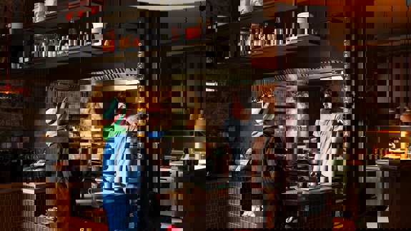 Interior of Outlier cafe with a chef and customer at the counter and an open kitchen. The place is dark and cosy in design.