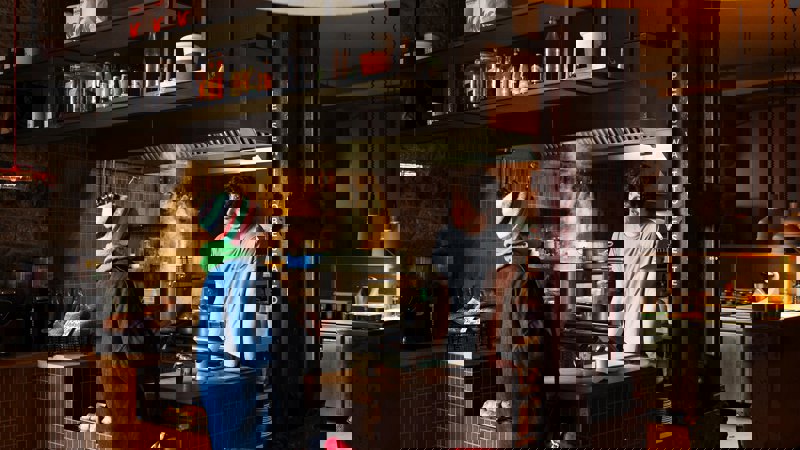 Interior of Outlier cafe with a chef and customer at the counter and an open kitchen. The place is dark and cosy in design.