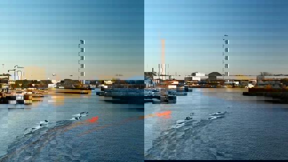 Two bright orange speedboats create ripples on the River Clyde with Glasgow Science Centre and the Glasgow Tower in the distance.