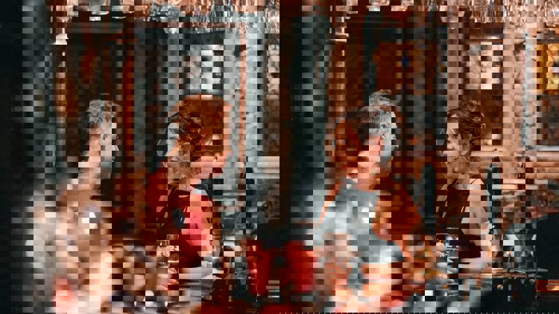 Two people sit at a traditionally decorated bar in conversation with each other, with rustic, exposed stone walls behind them.