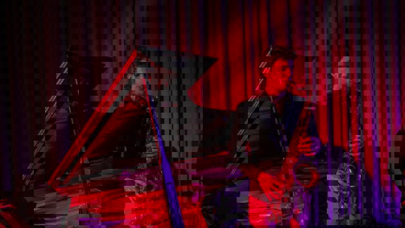 A saxophonist performs under red and purple lighting beside a grand piano at the University of Glasgow’s music department.