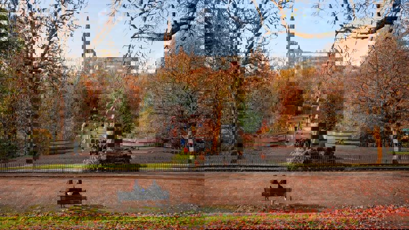 View of Kelvingrove Park in Glasgow during autumn, with people walking across the park bridge and the University of Glasgow tower visible in the background.