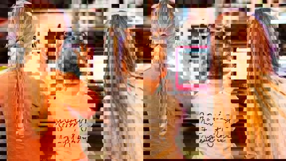 Three children sitting on a bench using electronic devices, with one wearing a shirt that says "growing together".