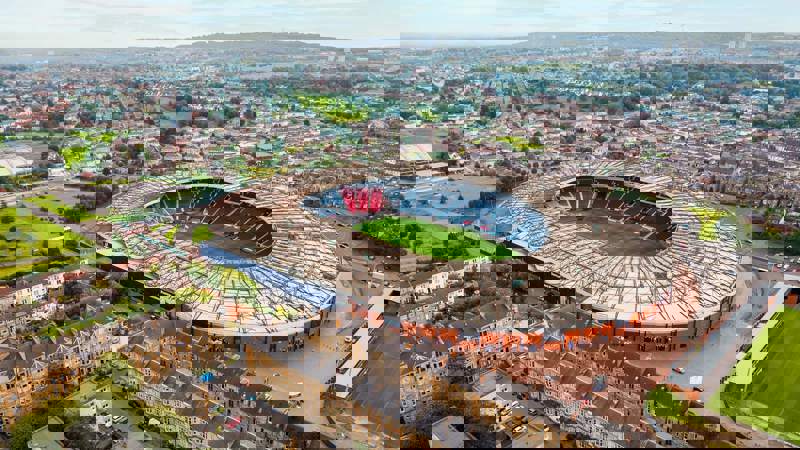 An aerial view of Hampden Park, a large, circular sports stadium, surrounded by residential areas and green space.