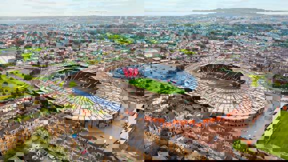 An aerial view of Hampden Park, a large, circular sports stadium, surrounded by residential areas and green space.