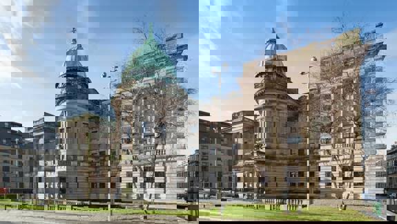 The imposing Mitchell Library in Glasgow, a grand building with a distinctive green dome and classical architecture, standing under a bright blue sky.