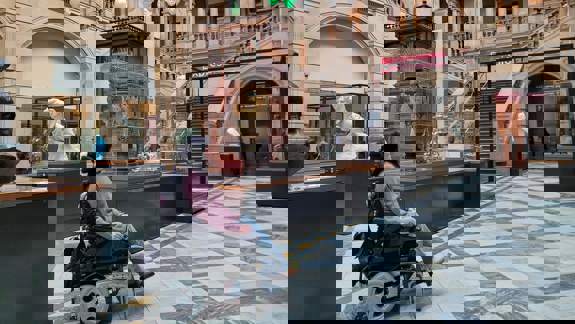 A person in a wheelchair inside the main hall of the Kelvingrove Art Gallery and Museum, with sculptures and a grand staircase in view.