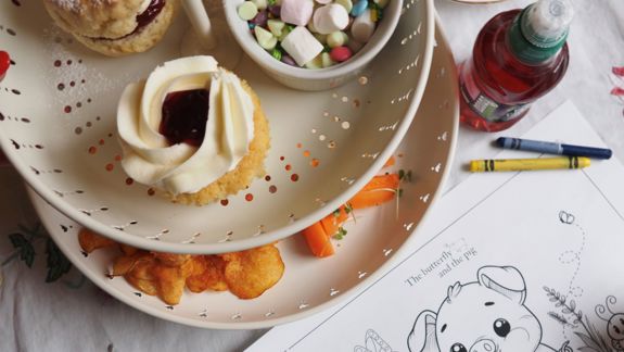 Tiered tray of treats including scones and crisps, with a colouring sheet and crayons beside it.