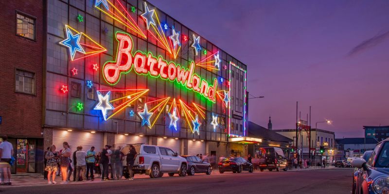 Exterior shot of Glasgow's Barrowland Ballroom at dusk, illuminated by vibrant neon lights spelling "Barrowland" amid shooting stars made of neon signage.
