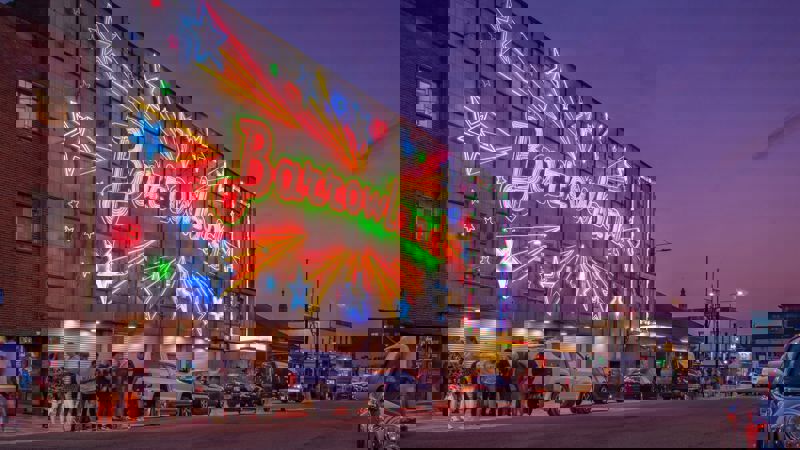 Exterior shot of Glasgow's Barrowland Ballroom at dusk, illuminated by vibrant neon lights spelling "Barrowland" amid shooting stars made of neon signage.