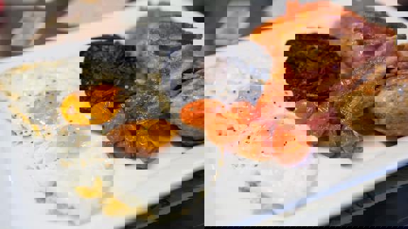 A plate with a full 'English' breakfast including two fried eggs, bacon, sausage, roasted tomatoes, and a mushroom.