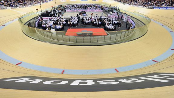 A view from above showing the Sir Chris Hoy Velodrome's wooden track. In the centre, a large crowd of people is seated at tables for a formal event.
