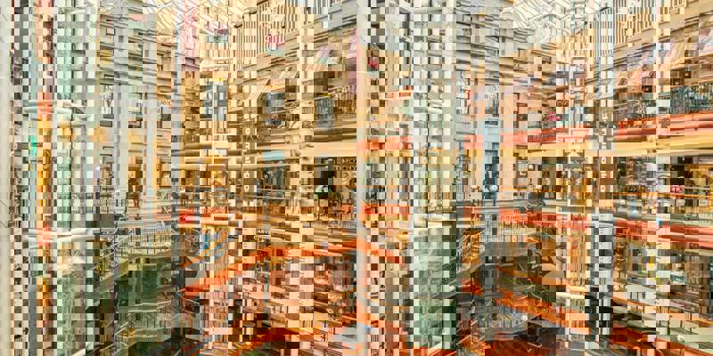 Interior view of Princes Square shopping center with multiple levels, escalators, and a glass roof.