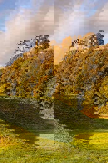 Stirling Castle sits majestically on a hilltop, surrounded by golden autumn foliage and a grassy mound in the foreground.