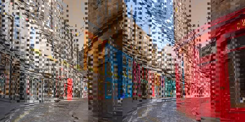 A curved cobblestone street in Edinburgh, lined with colourful, historic buildings housing small shops.