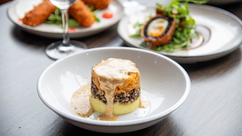 A plated tower of traditional haggis, neeps, and tatties, elegantly drizzled with a creamy whisky sauce.