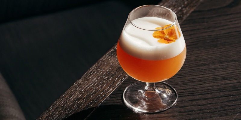 A close-up of a layered cocktail with an edible flower garnish on a wooden table.