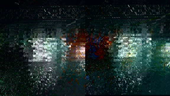 A crowd at SWG3 dances in front of a stage with a bright, abstract digital screen and surrounded by trees.