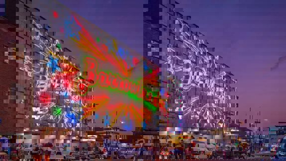 A vibrant, neon sign for the Barrowland Ballroom lights up a Glasgow street at dusk.