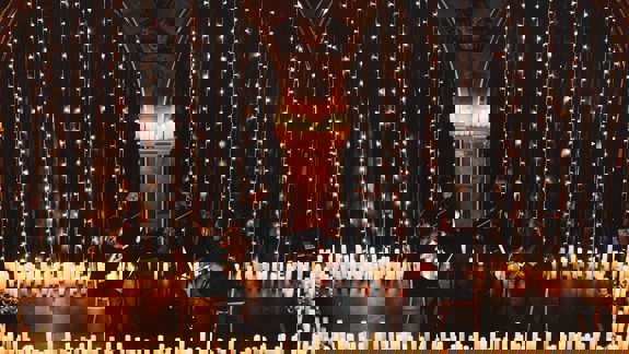 A string quartet performs surrounded by candles and fairy lights in Òran Mór, a former church venue with arched stone details.