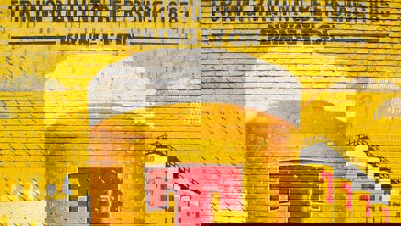 A vibrant yellow brick wall mural depicting a large beer glass with "Tennent's" and "Turning Rain into Beer Since 1885".