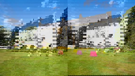 A white, two-story building with a dark roof and many windows sits on a green lawn with colourful, bell-shaped sculptures.