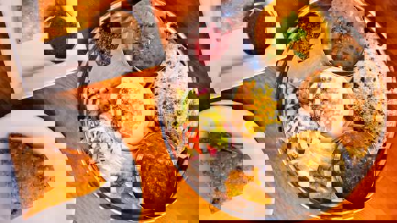 Overhead shot of a metal platter with Indian dishes, including curries, salad, roti, and samosas with chutney. Colourful, detailed presentation of traditional cuisine.