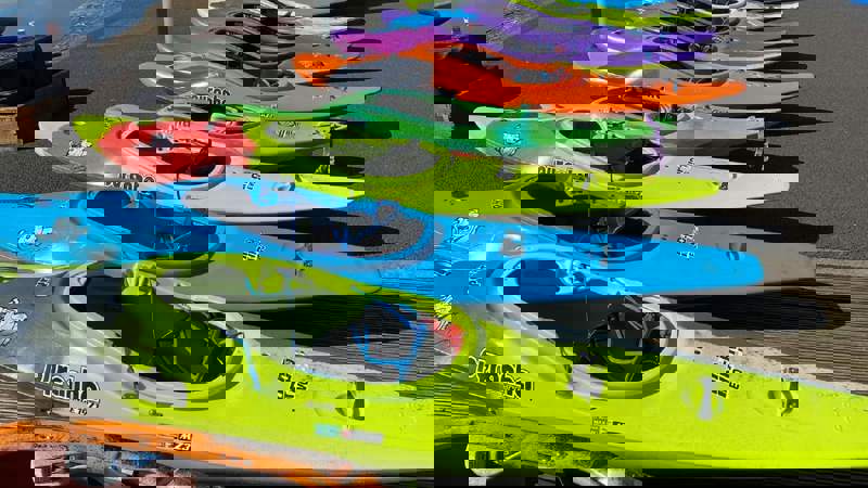 A row of colorful kayaks and canoes lined up on a wooden deck next to a body of water.