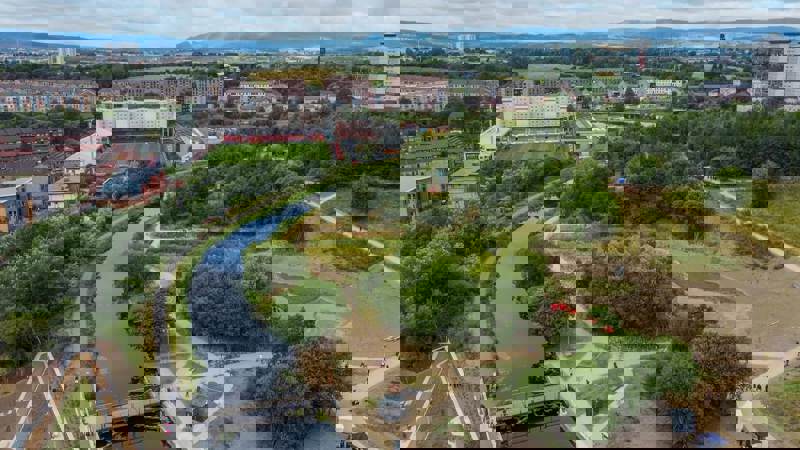 Aerial view of the Glasgow to Edinburgh canal route with footpaths, greenery, and the city skyline in the background.