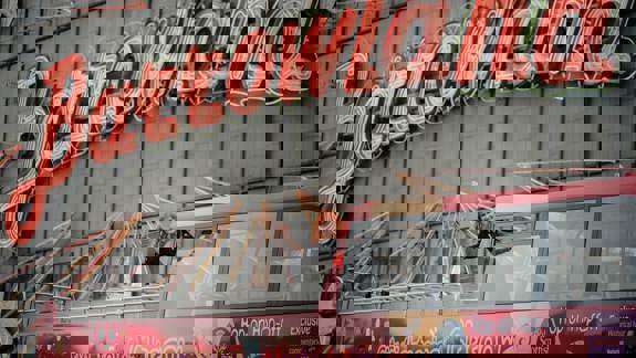 A red-haired woman waving from a red tour bus in front of the illuminated "Barrowland" sign.