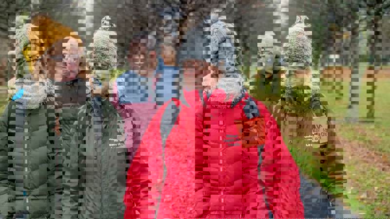 A group of adults of various ages walking down a path in a park during a community health walk.