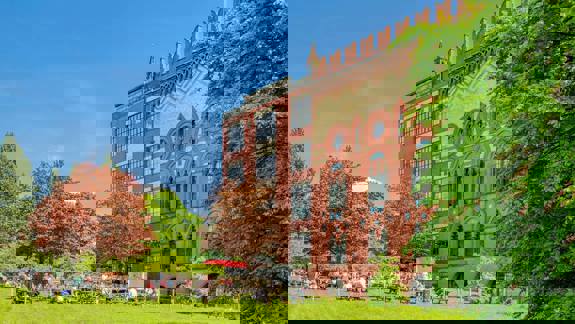 A large red brick building, West Brewery, with a beer garden on the grass in front of it filled with people.