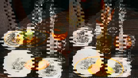 A dark wooden table set with four plates of artfully plated modern Scottish dishes, accompanied by wine and cocktails.