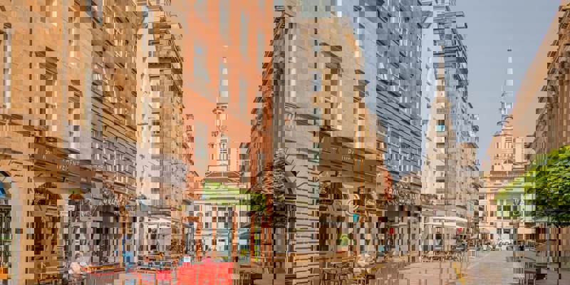 A street scene of stone buildings with shops and restaurants in Glasgow's Merchant City area.