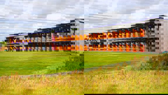 The two-storey driving range at Golf It! in Glasgow, with bright orange and purple practice bays overlooking the green fairway.