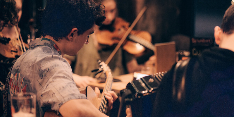 A group of young musicians plays traditional instruments in a cosy pub