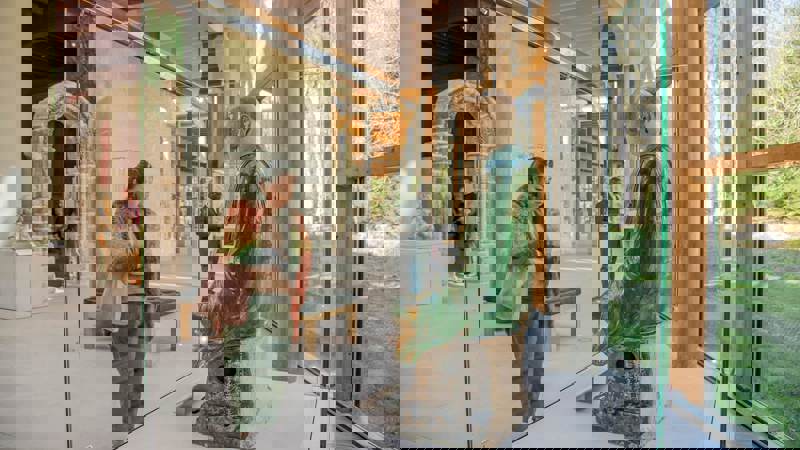 A woman looks at a green statue of a seated figure inside a museum.