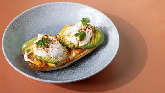 Plate of avocado toast topped with poached eggs, herbs, and seasoning at The Delphine restaurant in Glasgow