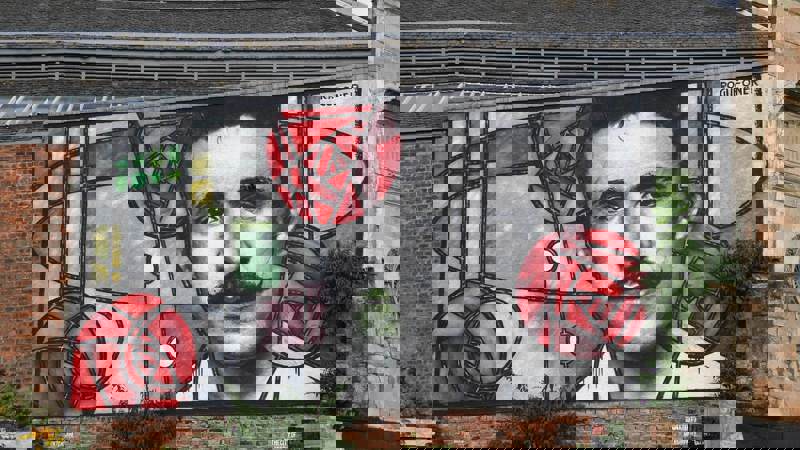 Colourful mural on a brick wall featuring bold geometric patterns and red roses, inspired by stained glass design, created by street artist Rogue-One.