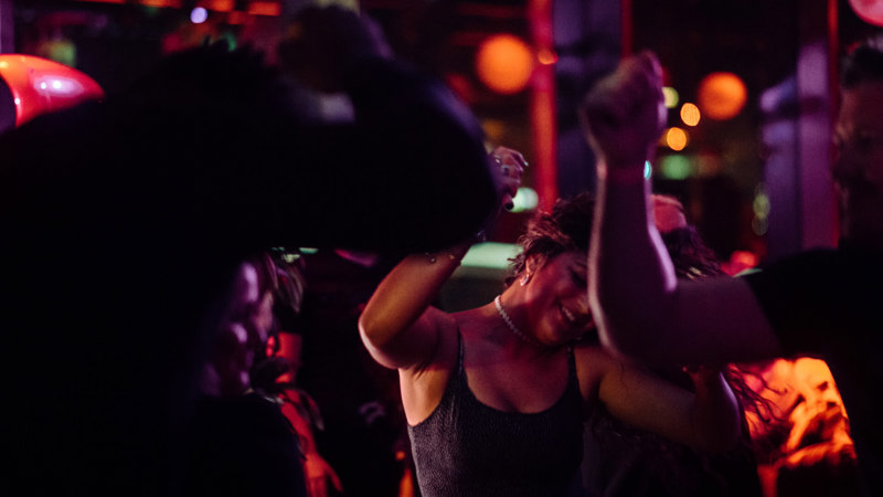 People dancing energetically under vibrant red and orange lights at a lively indoor party.