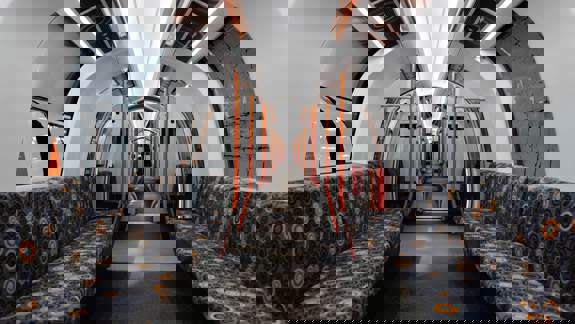 The interior of a modern, empty subway train features patterned seats, bright lighting, and sleek orange handrails.